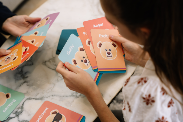 Child and adult using Tedology emotion cards spread across a table showing feelings like anger, guilt and excitement