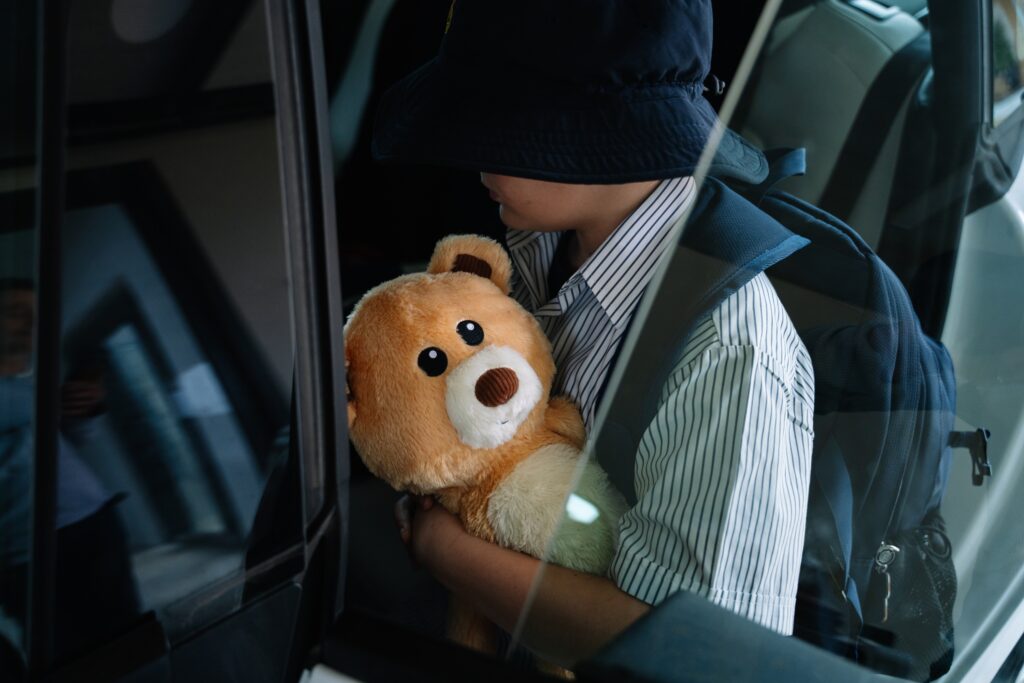 Young child in a car hugging a brown Tedology wellbeing bear on the way home from school